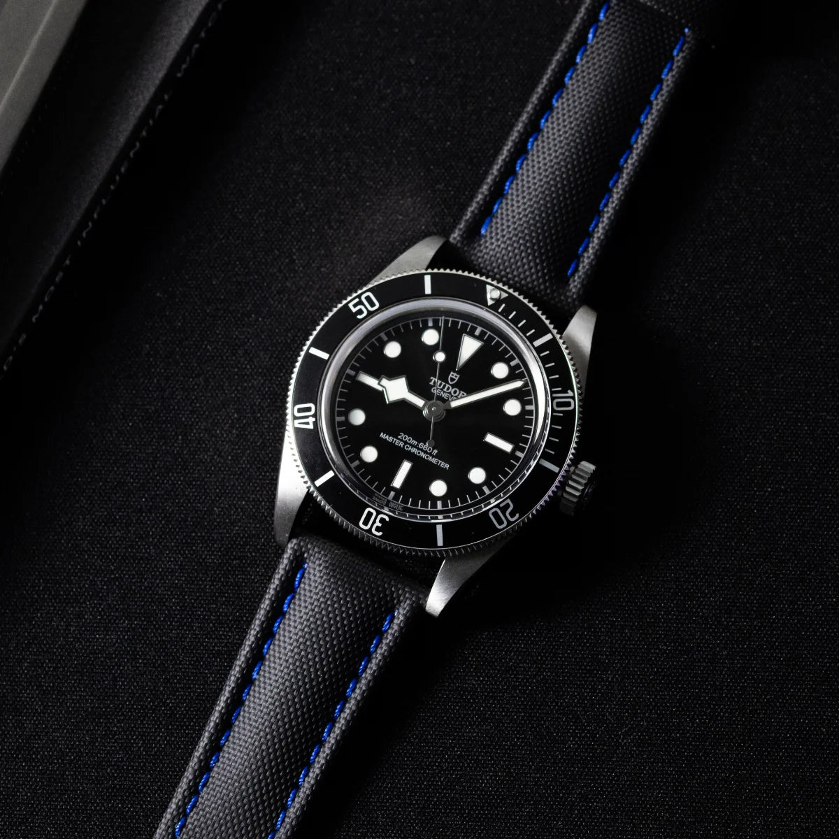 Watch with black dial and blue stitching on a dark background