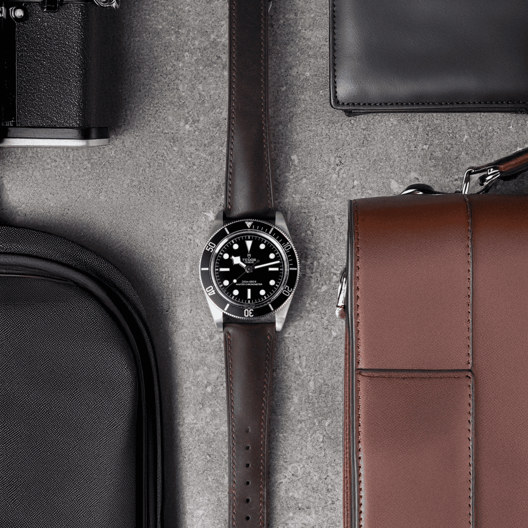 Watch with brown strap on a textured surface with bags and a wallet