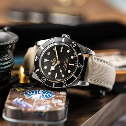 Watch with a black dial and beige strap on a wooden surface