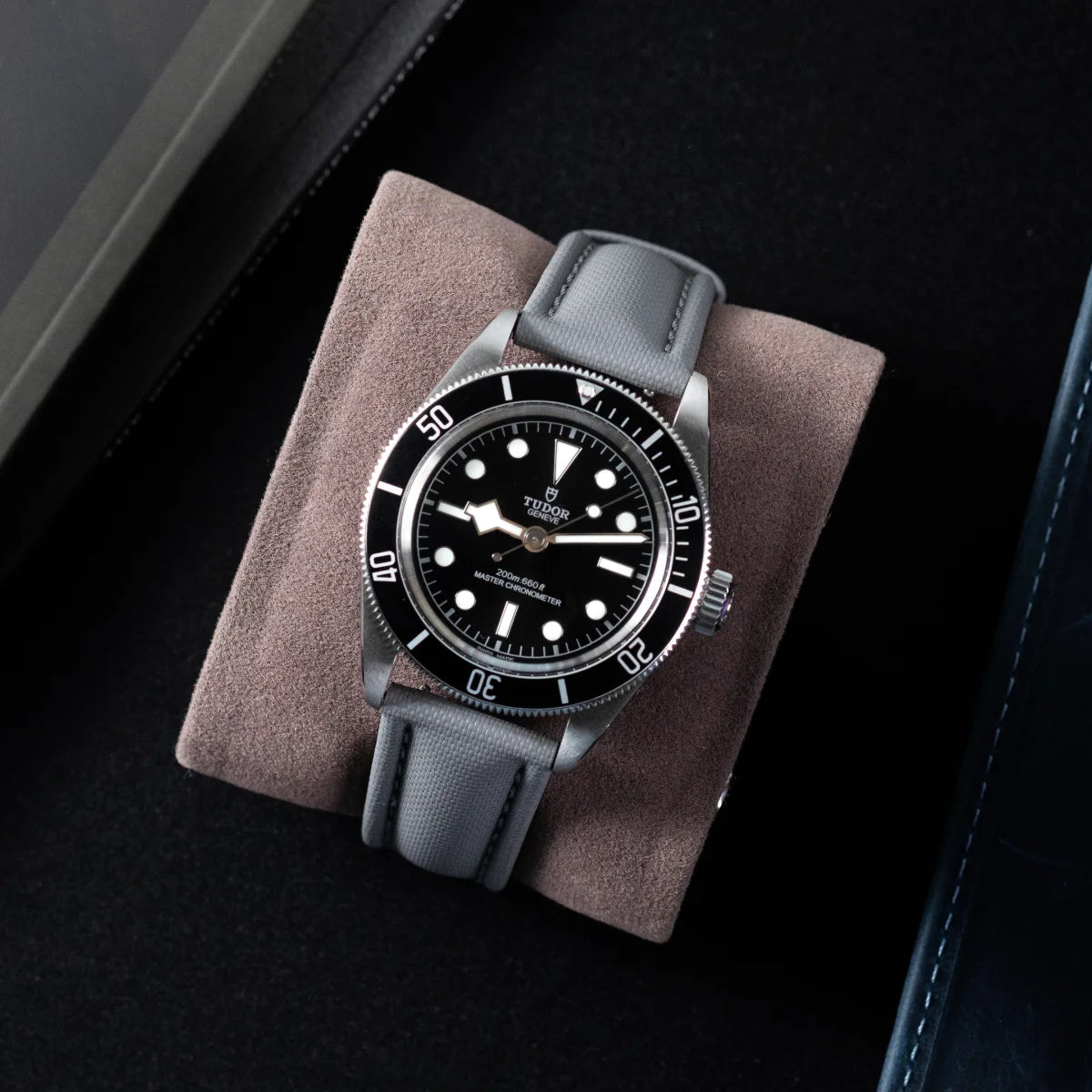 Watch with black dial and gray strap on a brown cushion against a dark background