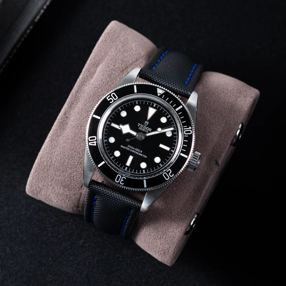 Watch with black dial and blue accents on a gray cushion against a dark background