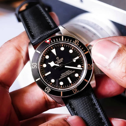 Close-up of a Tudor watch with a black strap held in hands